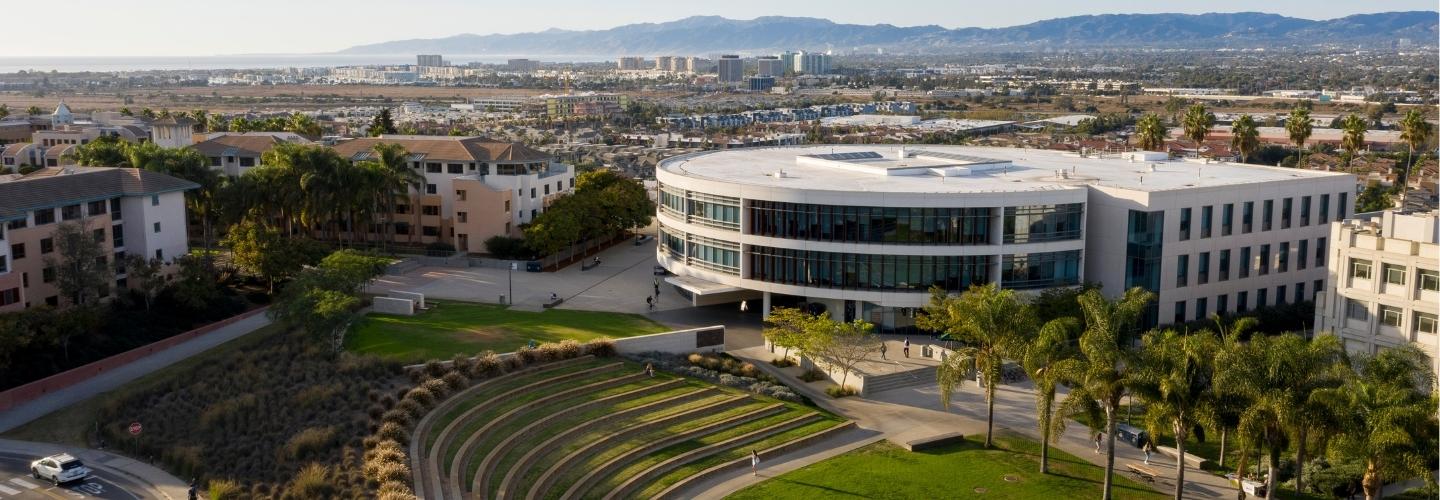 round concrete building and a terraced outdoor space in the foreground with other buildings in the distance